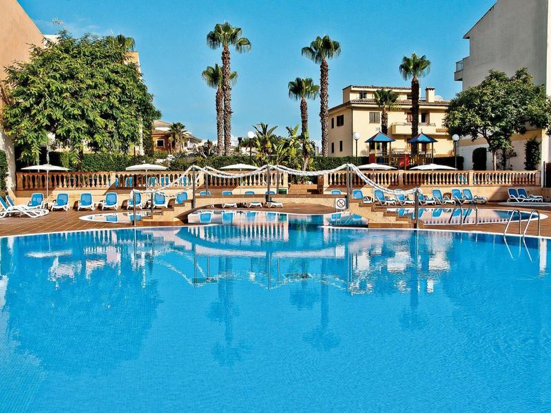 Gran piscina exterior con tumbonas azules y palmeras en el patio de un hotel bajo cielo despejado.