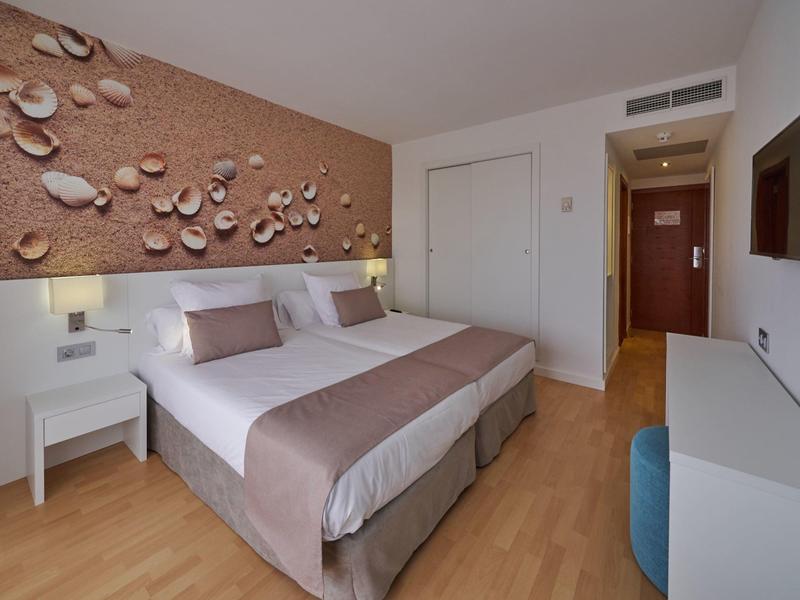 Habitación de hotel moderna con cama doble, suelo de madera y pared decorativa con conchas.