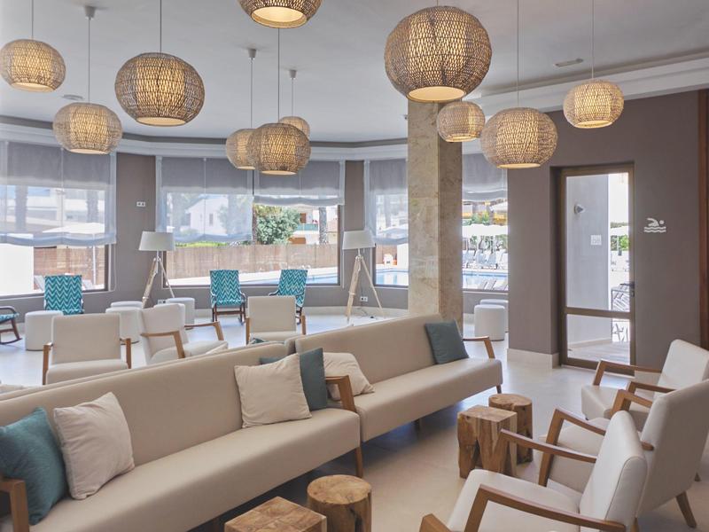 Sala de estar moderna de hotel con sofás cómodos, sillones y lámparas cálidas en tonos neutros.