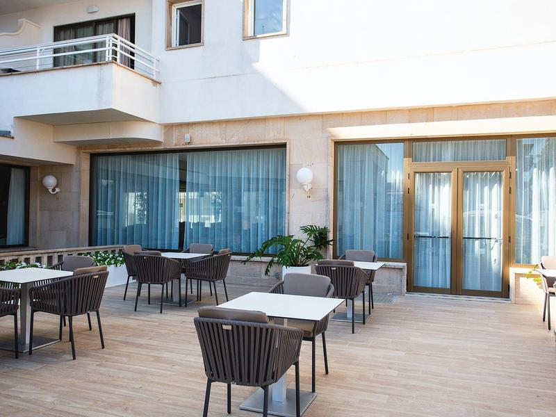 Moderna terraza exterior de un hotel con mesas y sillas sobre suelo de madera.
