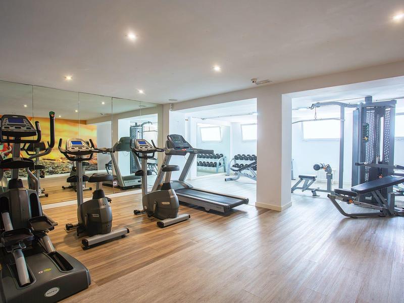 Gimnasio moderno con cintas de correr, pesas y máquinas de fuerza, suelo de madera clara.