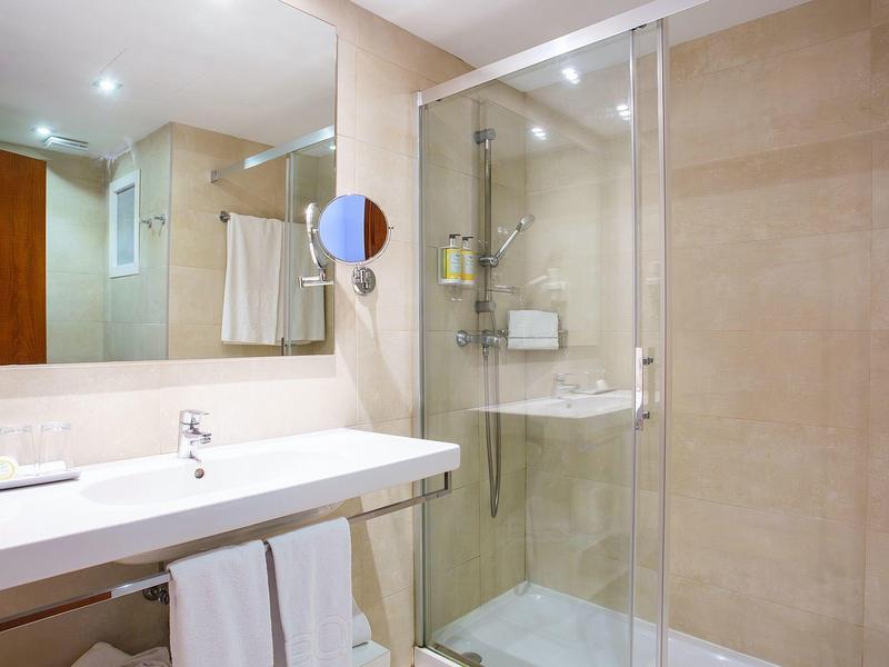 Baño moderno con ducha de vidrio, lavabo blanco y toallas, en tonos beige y luz cálida