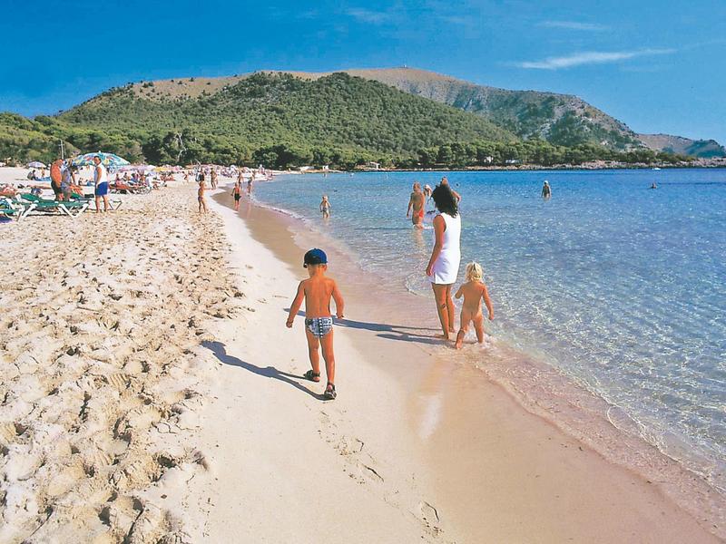 Famiglia cammina sulla spiaggia sabbiosa accanto al mare azzurro limpido in una giornata di sole.