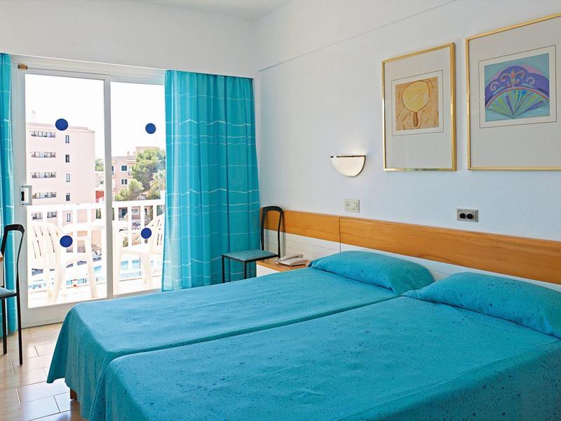 Camera d'hotel con due letti singoli, tende turchesi e balcone con vista sul mare.