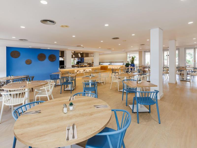 Ristorante luminoso con pavimento in legno, tavoli rotondi e sedie blu e bianche