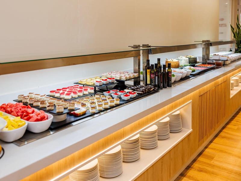 Lungo buffet con vari piccoli dolci e insalate in ciotole bianche su un piano bianco.