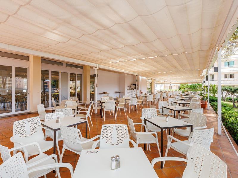 Area pranzo all'aperto con tavoli e sedie bianchi sotto una grande copertura.