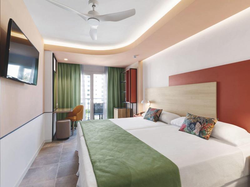 Habitación de hotel moderna con cama grande, cubrecama verde y balcón con cortinas.