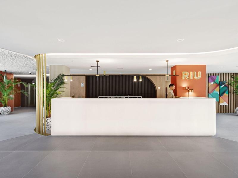 Área de recepción moderna y luminosa con mostrador blanco y plantas al fondo.