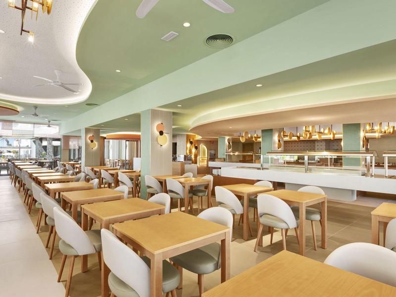 Comedor moderno y luminoso con mesas de madera y sillas blancas en un hotel.