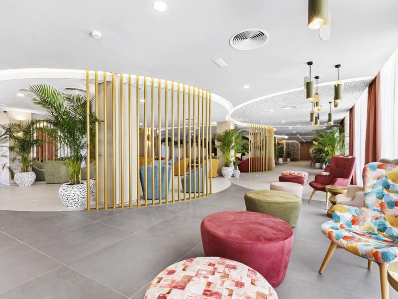 Área de descanso de hotel luminosa con sillones coloridos, plantas y elementos decorativos modernos.