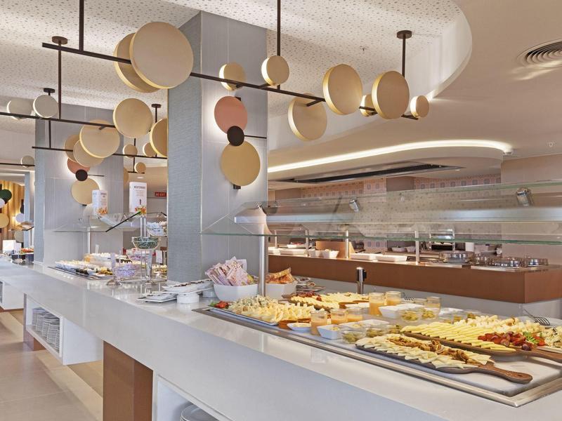 Buffet moderno de hotel con diferentes platos en un mostrador largo bajo lámparas de techo elegantes.