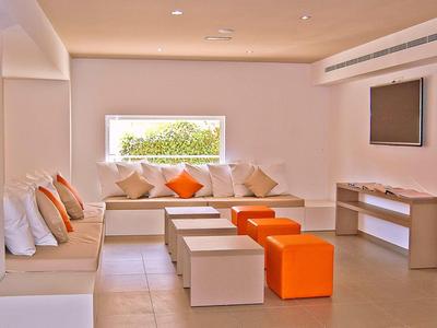 Nowoczesny salon hotelowy z białymi meblami i pomarańczowymi akcentami.