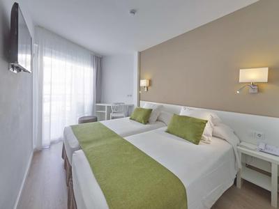 Camera d'albergo luminosa con due letti, accenti verdi e piccolo tavolo vicino alla finestra.