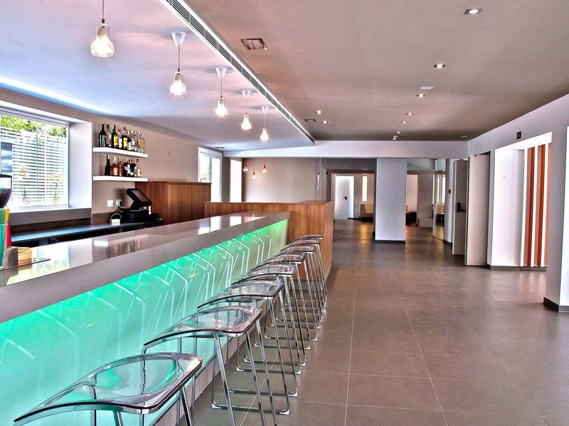 Nowoczesny bar hotelowy z podświetlanym kontuarem i przezroczystymi stołkami barowymi.