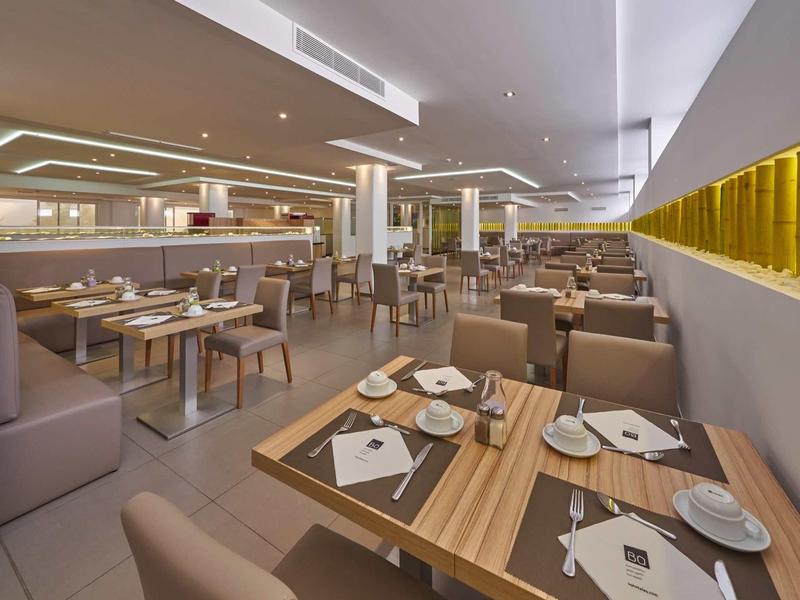 Nowoczesna restauracja hotelowa z drewnianymi stołami, brązowymi krzesłami i nakrytymi stołami w jasnej atmosferze.