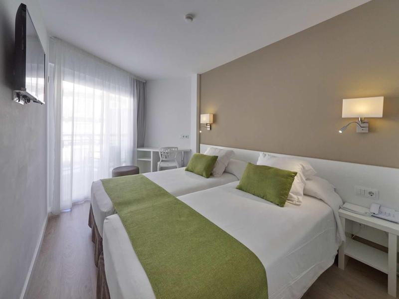 Nowoczesny pokój hotelowy z dwoma pojedynczymi łóżkami, zielonymi akcentami i oknem z zasłonami.