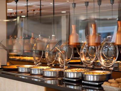 Buffet mit warmen Speisen, Teller und aufgereihten Weingläsern unter hängender Beleuchtung.