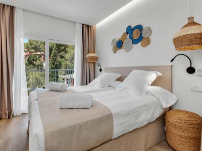 Helles Schlafzimmer mit Doppelbett, weißer Bettwäsche, beige Deko und großem Fenster mit Vorhängen.