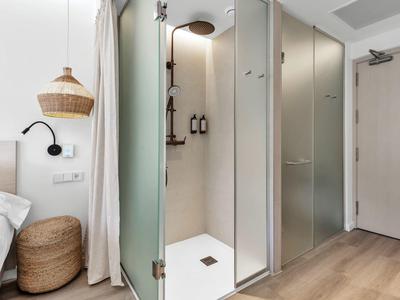 Kleine, moderne Dusche mit Milchglasscheiben, weißem Badezimmer und Holzboden neben einem Bett und Korb.
