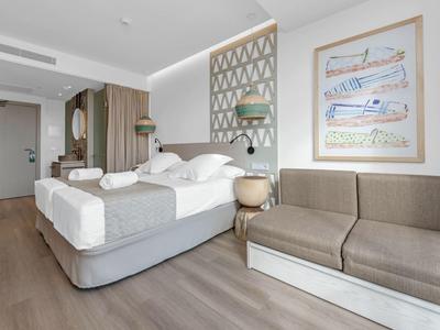 Modernes Hotelzimmer mit Doppelbett, grauem Sofa, hellem Holzfußboden und Kunst an der Wand.