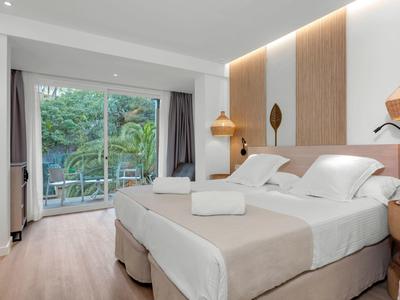 Helles Schlafzimmer mit Doppelbett, Holzpaneelen und Gartenblick durch große Fenstertür.