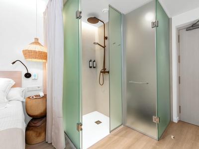 Modernes Badezimmer mit dusche aus Glas, hölzernem Nachttisch und weißem Bett im Hintergrund.