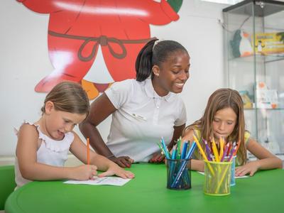 Drei Kinder sitzen an einem grünen Tisch und malen konzentriert mit bunten Stiften.