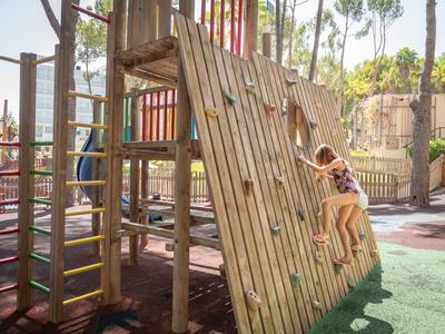 Kinder klettern an einer schrägen Kletterwand auf einem bunten Spielplatz im Freien.