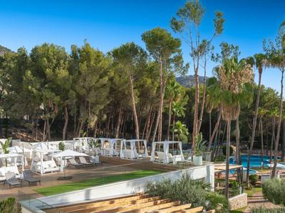 Moderner Außenbereich mit weißen Loungemöbeln, Pools und hohen Bäumen unter blauem Himmel.