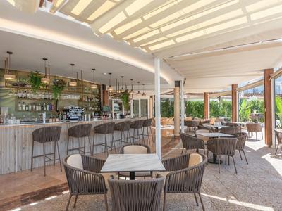 Moderner Außenbereich einer Bar mit Holztischen, geflochtenen Stühlen und viel natürlichem Licht.