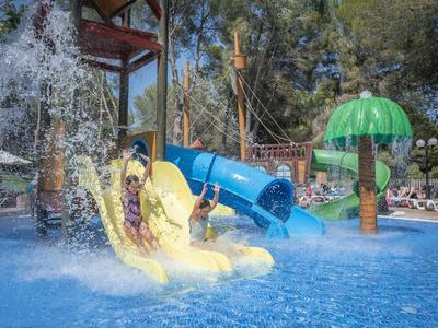 Kinder rutschen mit Spaß auf gelben und blauen Wasserrutschen in einem Pool mit Wasserfontäne.