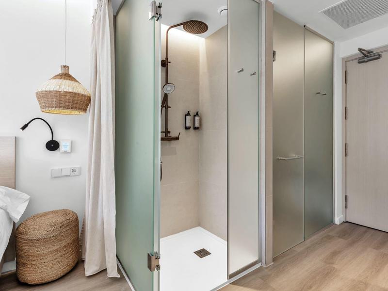 Moderní vstup do hotelového pokoje se sprchovými dveřmi ze skla a přírodní dekorací.