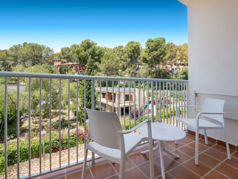 Balkon s bílými židlemi a stolem s výhledem na stromy a modrou oblohu.