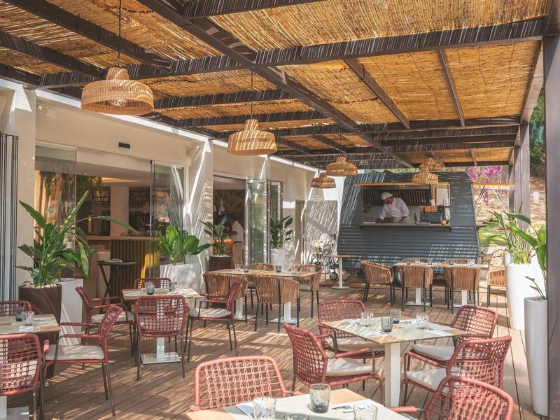 Pohodlná venkovní terasa restaurace s dřevěným stropem a ratanovými židlemi.