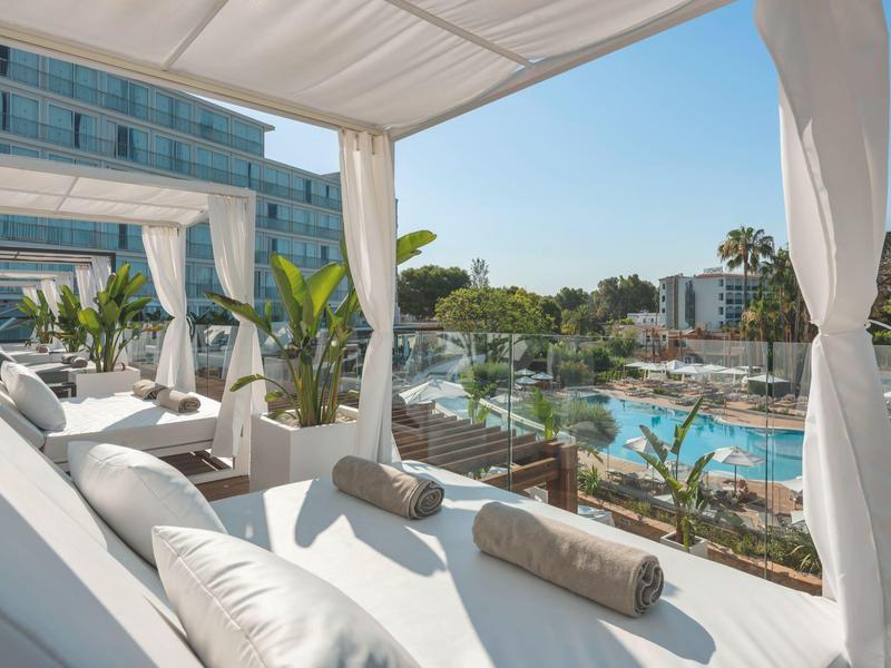 Luxusní balkon s pohodlnými denními postelemi s výhledem na velký hotelový bazén a zahradu.