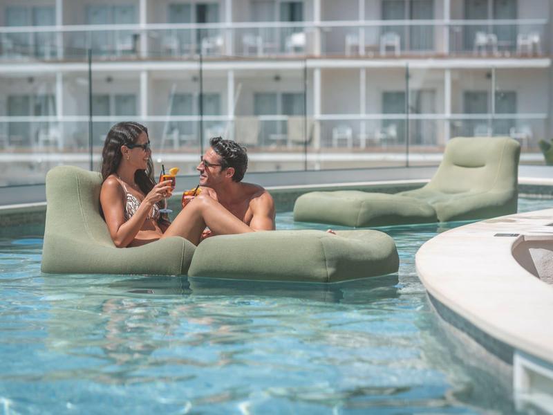 Dvě ženy odpočívají na plovoucích pohovkách v hotelovém bazénu a užívají si nápoje.