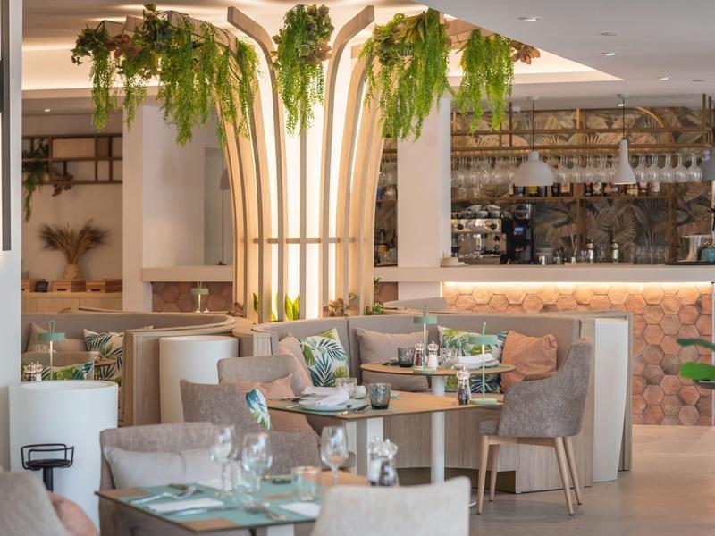 Moderně zařízená restaurace s rostlinami na centrálním osvětleném sloupu a stylovými stoly.