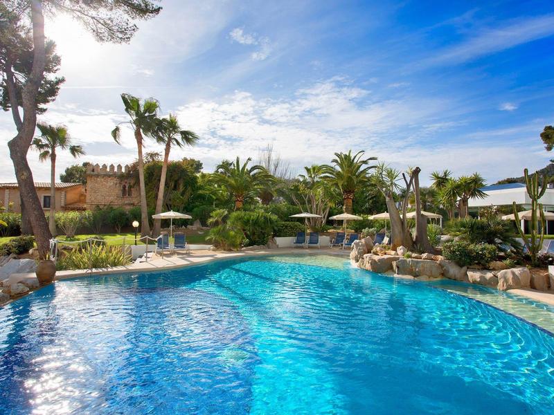 Čirý modrý bazén ve stylu laguny s palmami a lehátky v tropickém hotelovém resortu.