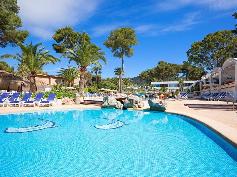 Čistý venkovní bazén s lehátky, palmami a modrou oblohou v hotelovém resortu.