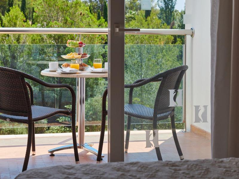 Balkon se dvěma židlemi a stolem s nápoji a občerstvením, výhled na zelené stromy.