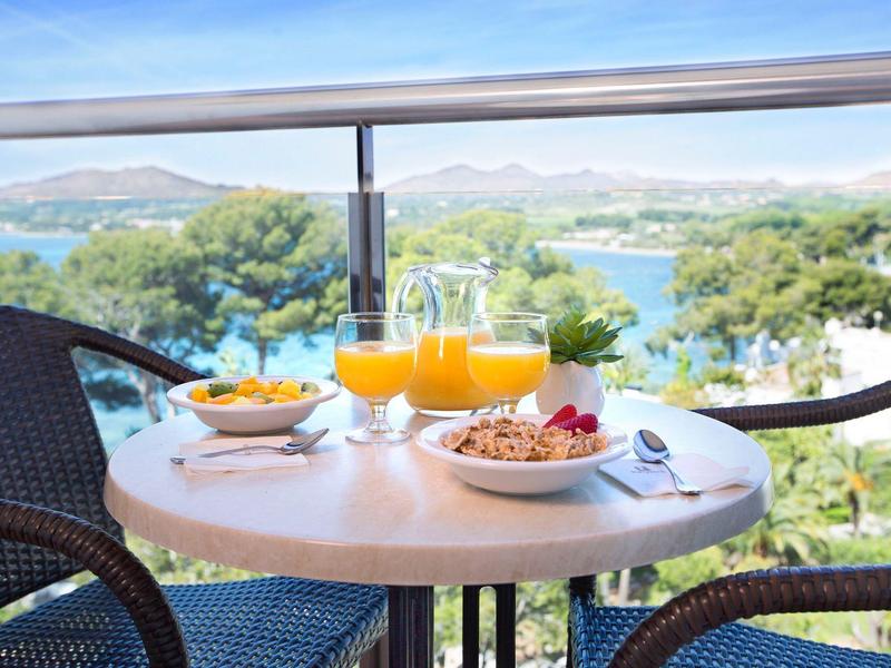 Malý stůl na balkoně se snídaní a širokým výhledem na moře za slunečného počasí.