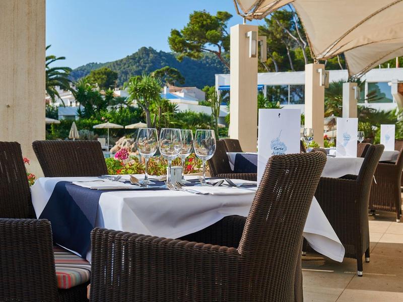 Venkovní stůl s nádobím a sklenicemi pod bílým baldachýnem v hotelové zahradě.