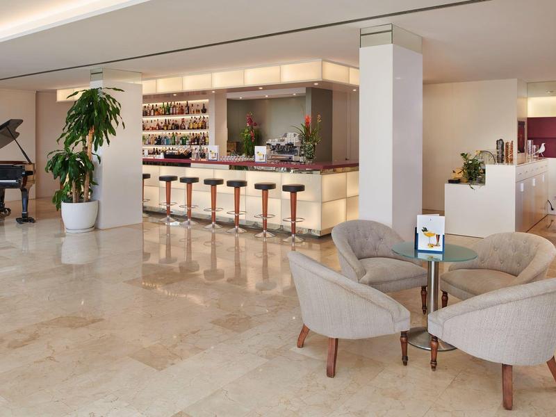 Světlý hotelový lobby prostor s barem, pohovkami, křesly a černým křídlem.
