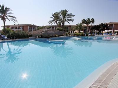 Large hotel pool with palm trees and sun loungers on a sunny day