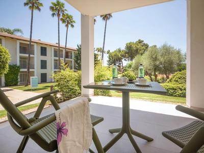 View from a terrace with chair and table overlooking a garden with palm trees and hotel building.