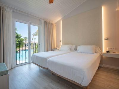 Modern hotel room with two beds and a pool view through large windows.