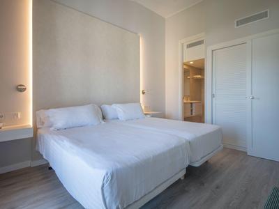 Modern hotel room with two single beds, white walls, and minimalist design.