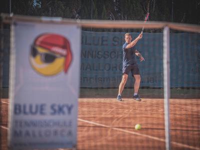 Uomo che gioca a tennis su campo in terra battuta dietro uno striscione con logo occhiali da sole