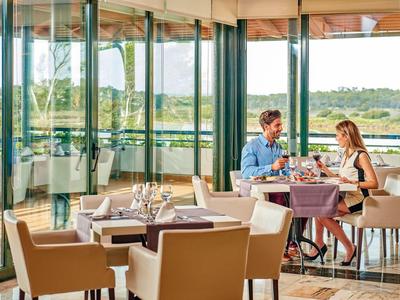Coppia seduta a un tavolo apparecchiato in un ristorante moderno con grandi vetrate che si affacciano sulla natura.